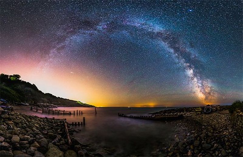 The milky way is seen forming an arch shape over the sea.