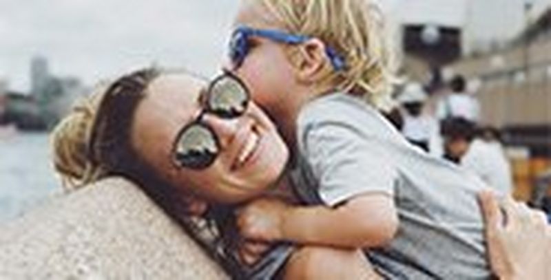 A mother picks her son up to hug, both of them wearing sunglasses. Photo by Christian Anderl.