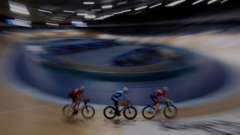 Three cyclists ride around a velodrome; the cyclists are in sharp focus, with everything else blurred.