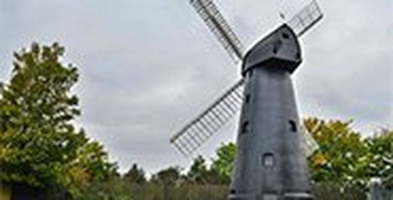 A windmill against a green countryside background on a cloudy day.