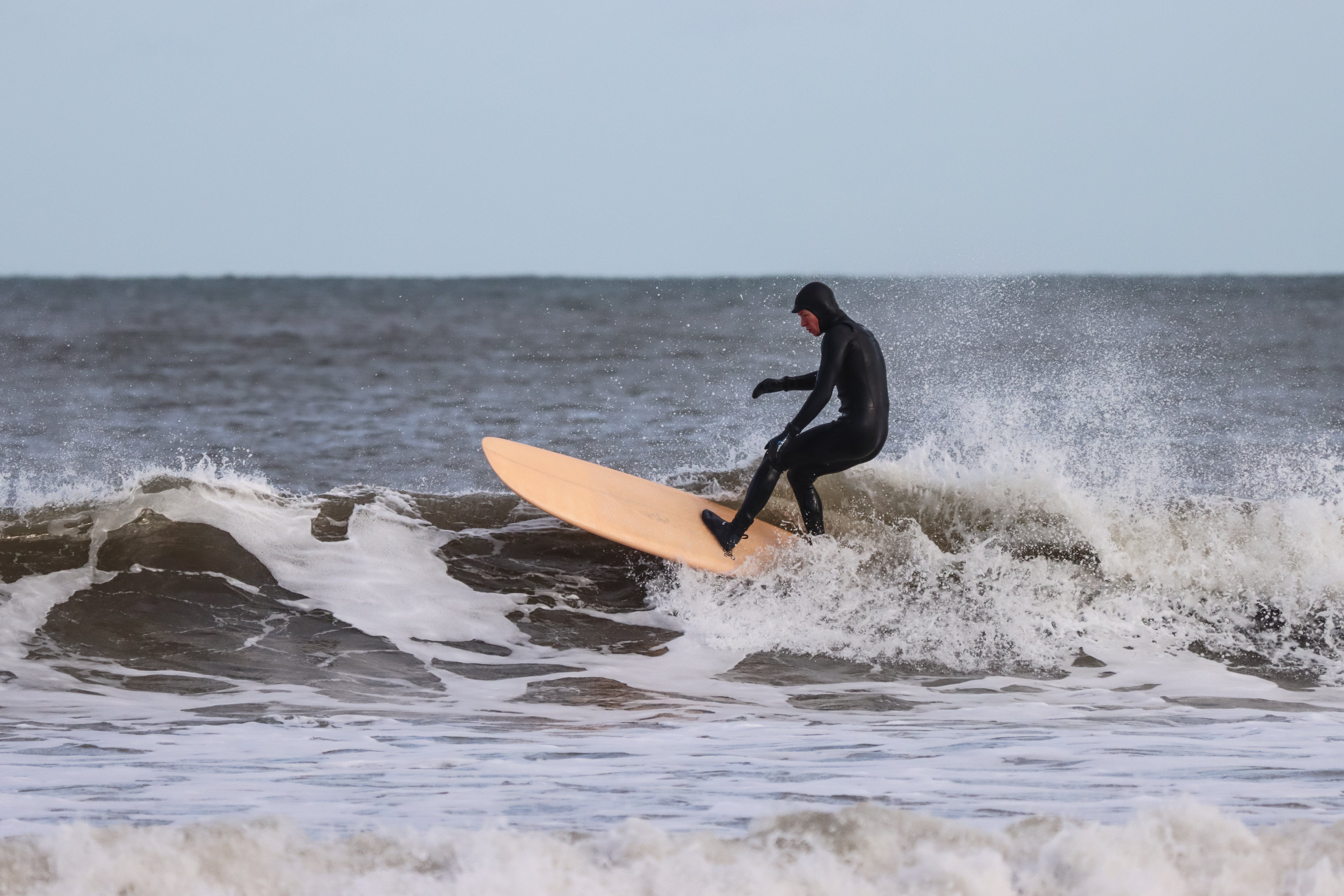 A surfer in a black wetsuit catches a wave as spray breaks around him.