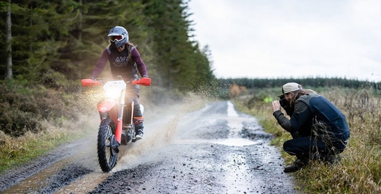 A dirt bike heads towards the camera spraying muddy water in its wake.