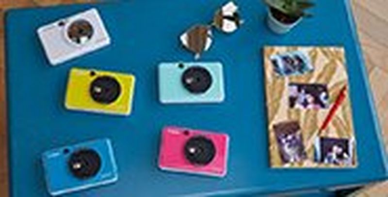 Canon Zoemini C and Canon Zoemini S on a table with a notebook with pictures stuck to it.