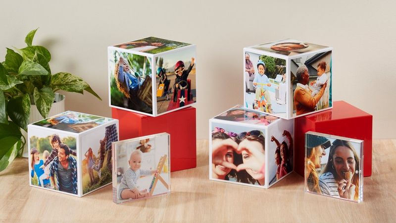 Plusieurs Canon Photo Cubes, certains empilés les uns sur les autres, sur une table en bois avec une plante verte dans le coin.