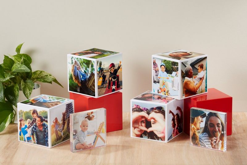 Flere Canon Photo Cubes, nogle stablet oven på hinanden, på et træbord med en grøn plante i hjørnet.
