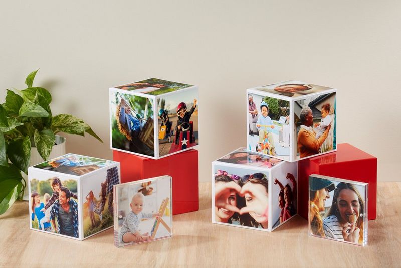 Several Canon Photo Cubes, some stacked on top of each other, on a wooden table with a green plant in the corner.