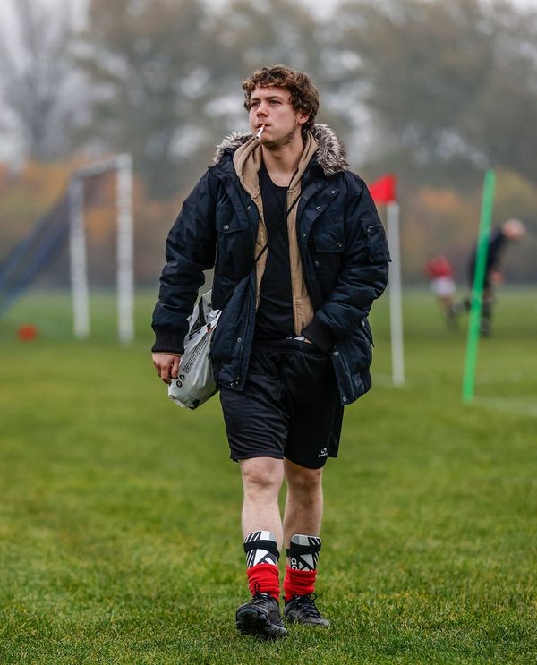 An amateur football player walking away from the pitch, smoking a cigarette. 