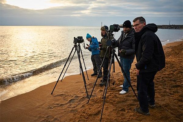 Helen Bartlett, David Noton, Sanjay Jogia and Eddie Keogh taking photographs on the beach at dusk.