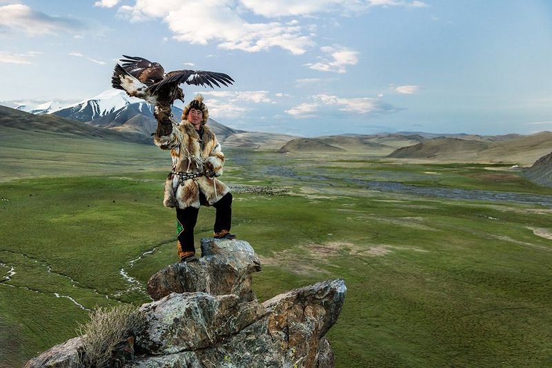 A Kazakh man holding an eagle in front of a mountain landscape. Photo by Joel Santos on a Canon EOS 5DS R.