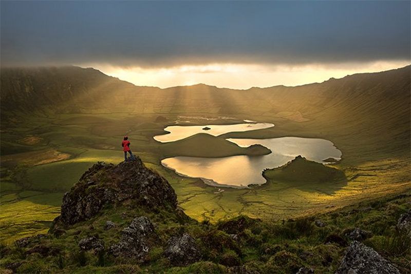 A person stands on a cliff overlooking a volcanic crater on the island of Corvo, Portugal. Photo by Joel Santos on a Canon EOS R.