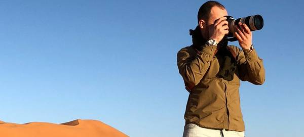 Antonio Gibotta holds his Canon DSLR to his eye in a bright desert setting.