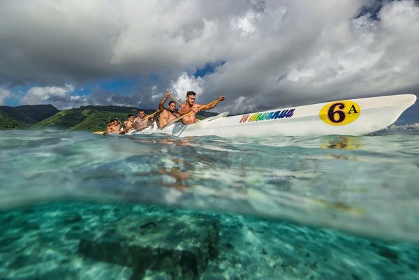 A split shot of a Tahitian canoe gliding through the water, showing detail above and below the waterline.
