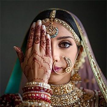 An Indian bride holds a henna-covered hand over one eye.