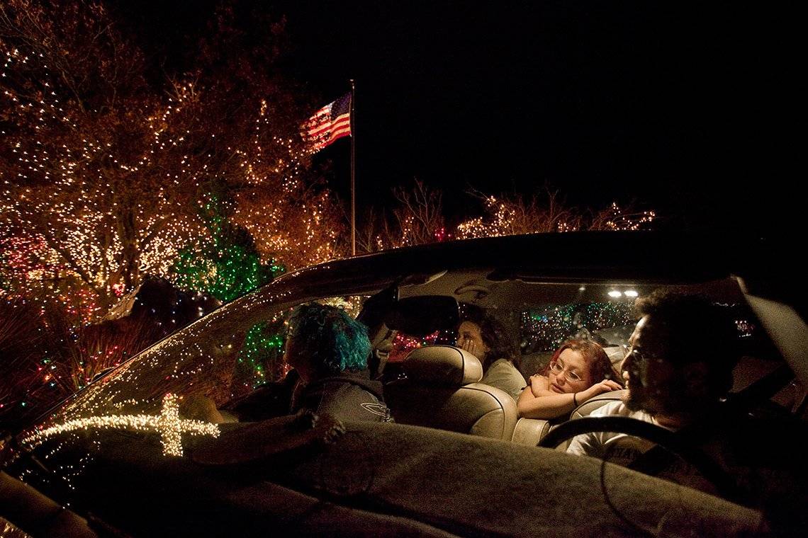 A family of four sit in a car with a creamy-coloured leather-upholstered interior, looking at Christmas lights, some of which are reflected in the windscreen of the car.