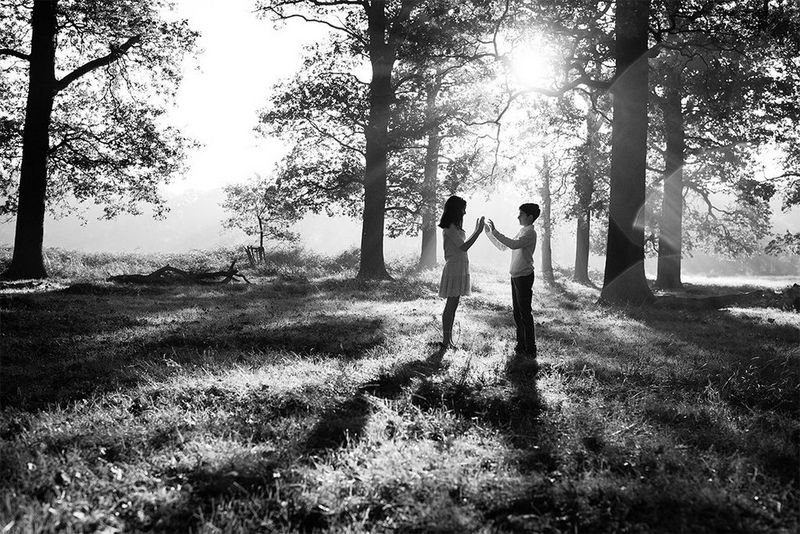 In a woodland clearing, a young boy and girl are standing facing each other. 