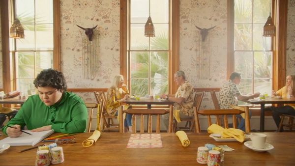 A still from a healthcare advert shot by Alice Gu of a teenage girl in a green shirt sat at a long dining table.