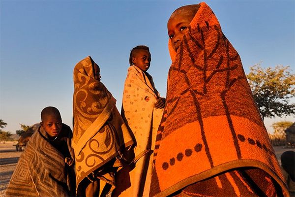 Four Himba boys drape themselves in predominantly ochre and dun coloured wraps with bold patterns.
