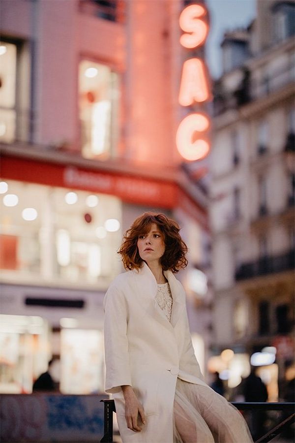 A bride wears a white coat in a city. Photo by Félicia Sisco with a Canon RF 85mm F1.2L USM lens.