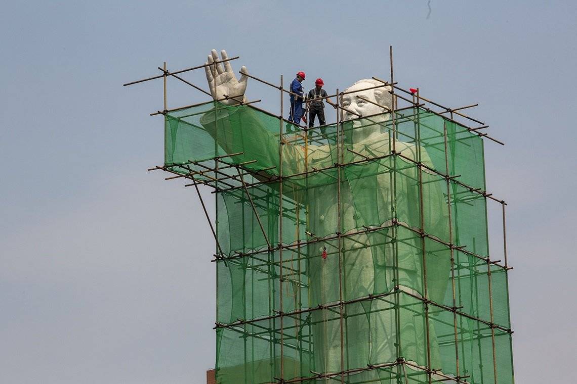 A statue of Mao Zedong covered in scaffolding with two construction workers standing on top.