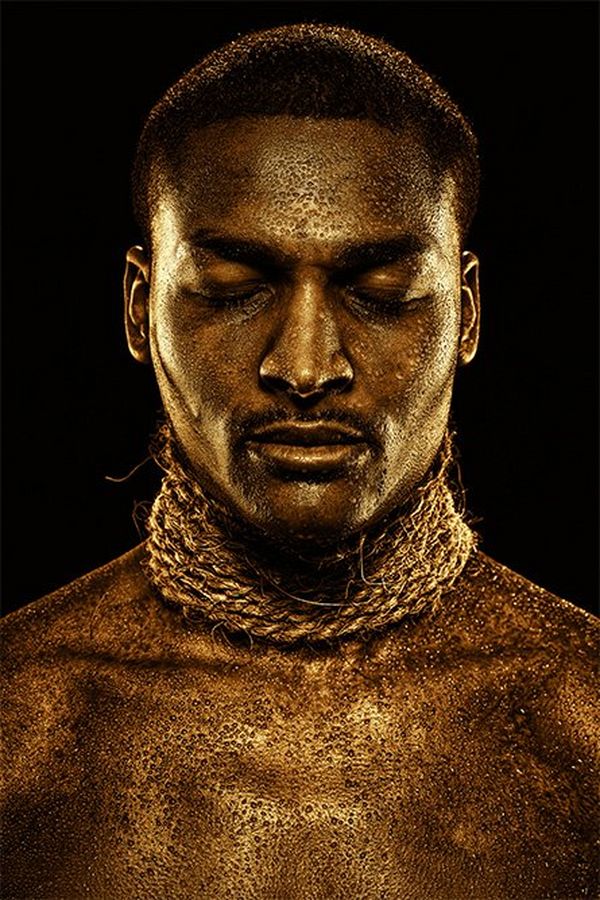 A man with gold-painted skin wears strings of rope around his neck.