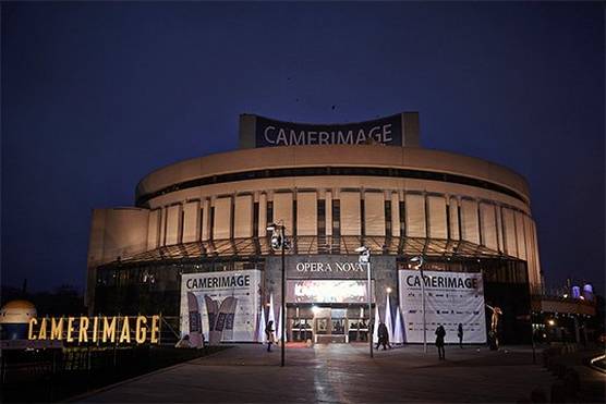 The round, concrete Opera Nova building is seen with a red carpet leading up to its doors, with signs saying 'CAMERIMAGE'.
