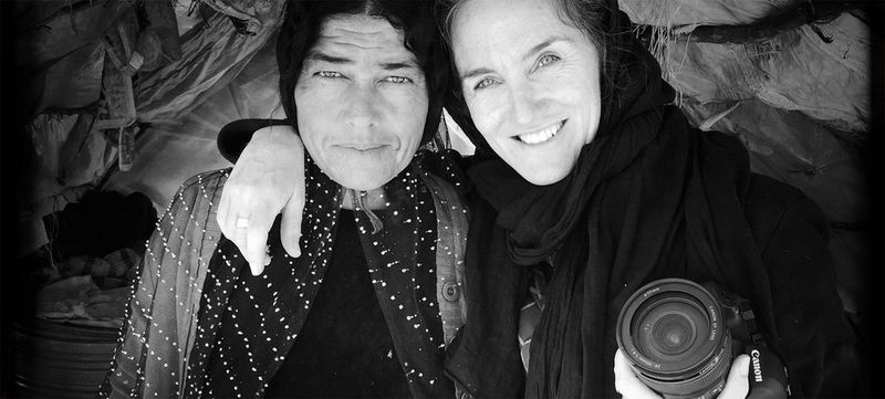 Photographer Catalina Martin-Chico stands inside a tent with her arm around a female Iranian nomad and holding a camera. Both smile.