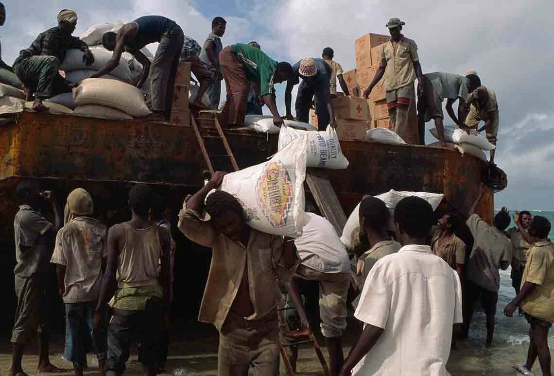 Men unload large sacks from the top of a bus.