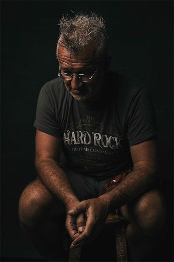 A man with greying hair and steel-rimmed glasses sits with elbows on his knees looking pensively downwards.