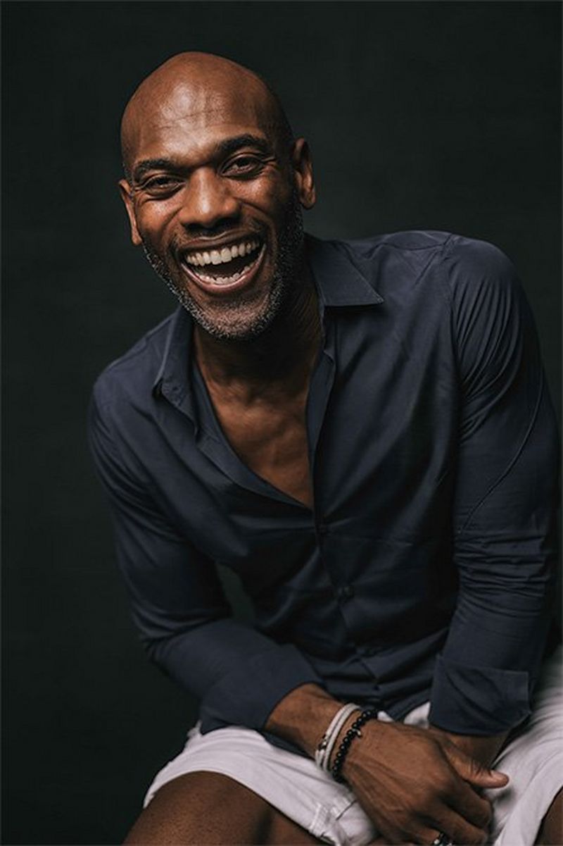 A man in a dark blue shirt and white shorts leans forward, laughing broadly.