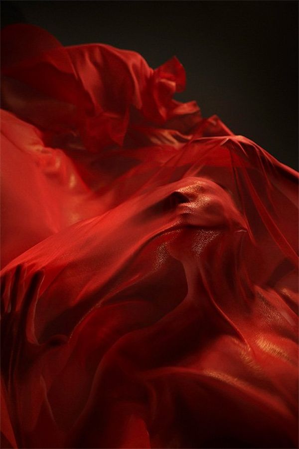 A ballet dancer shrouded in fluttering red silks, photographed from below.
