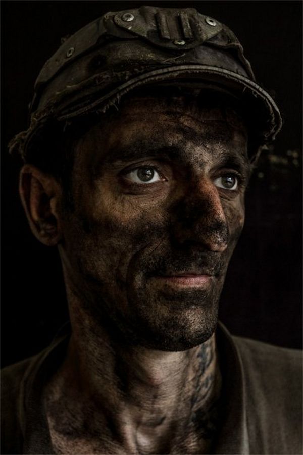 A portrait of a miner looking to his left, with a solemn look and black coal dust covering his face.
