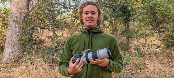 Daniël Nelson stands in front of a wood holding a Canon camera with telephoto lens.