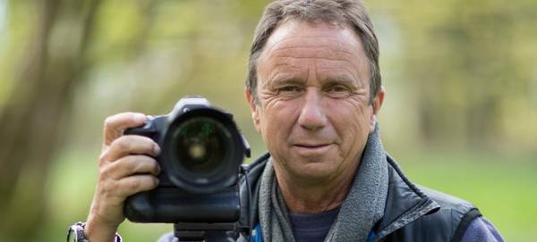 David Noton with a Canon DSLR as he stands in a woodland.