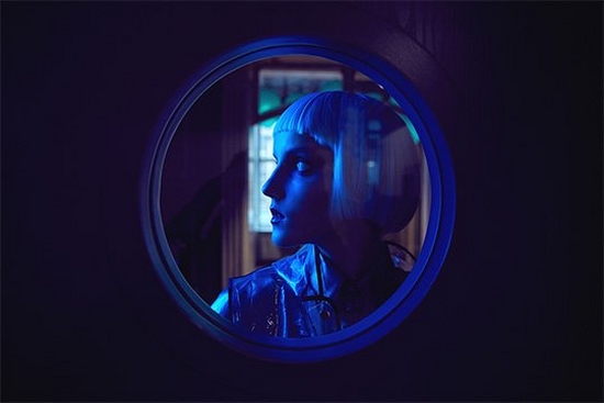 A profile of a woman behind a circular window, shot with a blue gel filter. Taken by Jaroslav Monchak.