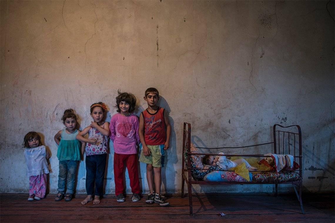 Six siblings pose for a portrait against a bare wall in a sparsely-furnished room. Photo by Anush Babajanyan