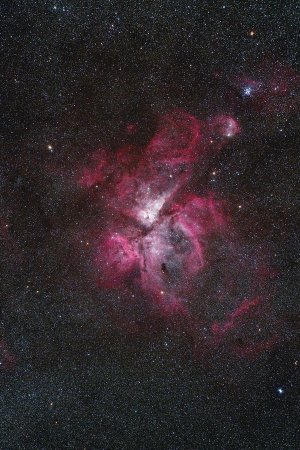 A swirling pink nebula shines through the dark sky dotted with stars.