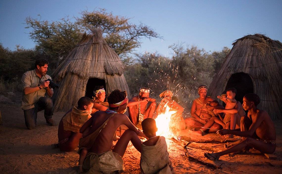 Brent Stirton photographs Namibian tribespeople by the fire, as Spencer MacDonald films him using a Canon EOS C200.