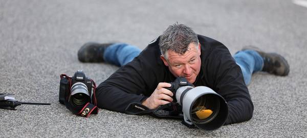 Sports photographer Frits van Eldik lying prone on a racetrack with a Canon EOS-1D X Mark II camera and telephoto lens.