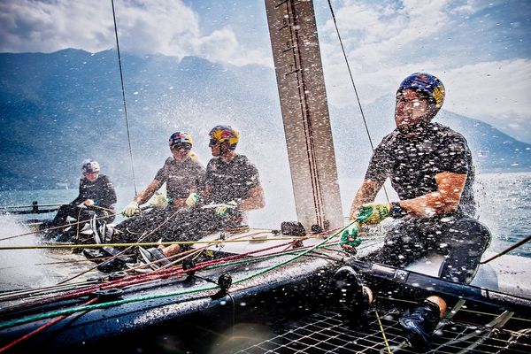 Four men on a racing catamaran bracing against the spray from the sea.