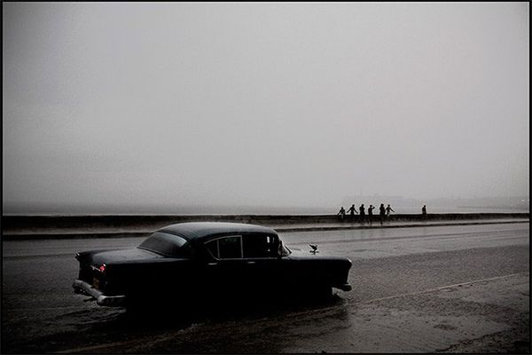 An old car drives through a large puddle in the rain on Havanas seafront road, the Malecon.