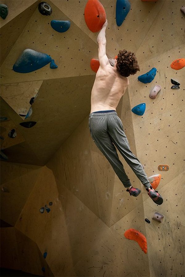 Declan Rounthwaite hangs by one hand from a climbing wall, body arcing gracefully to one side.