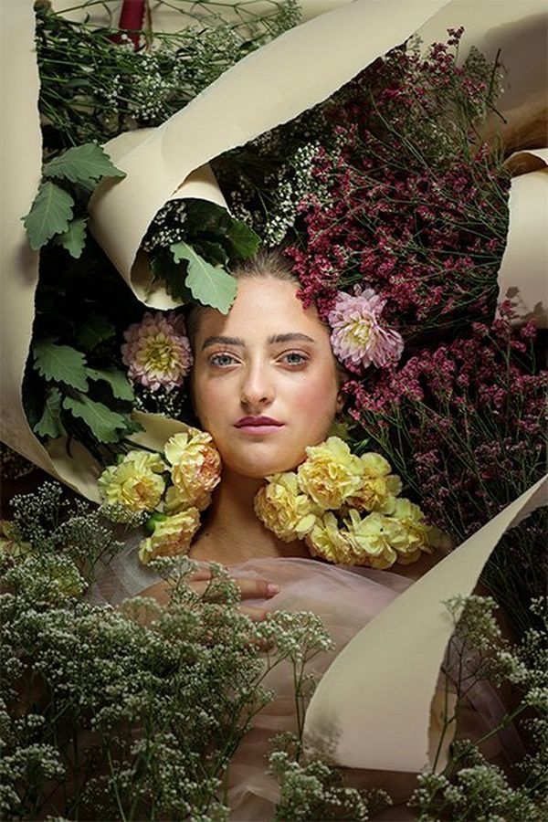 A white models face appears among flowers as she lies on the floor with twists of torn paper also arranged around her.
