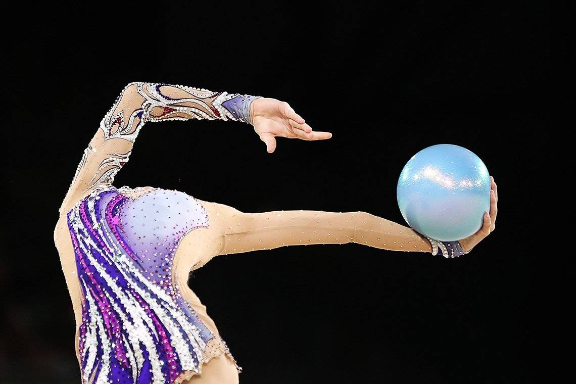 A gymnast holding a ball appearing headless 