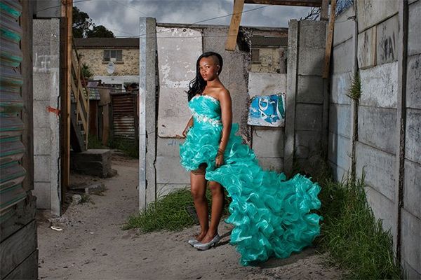 A girl stands in an elaborate prom dress next to a concrete-block wall.