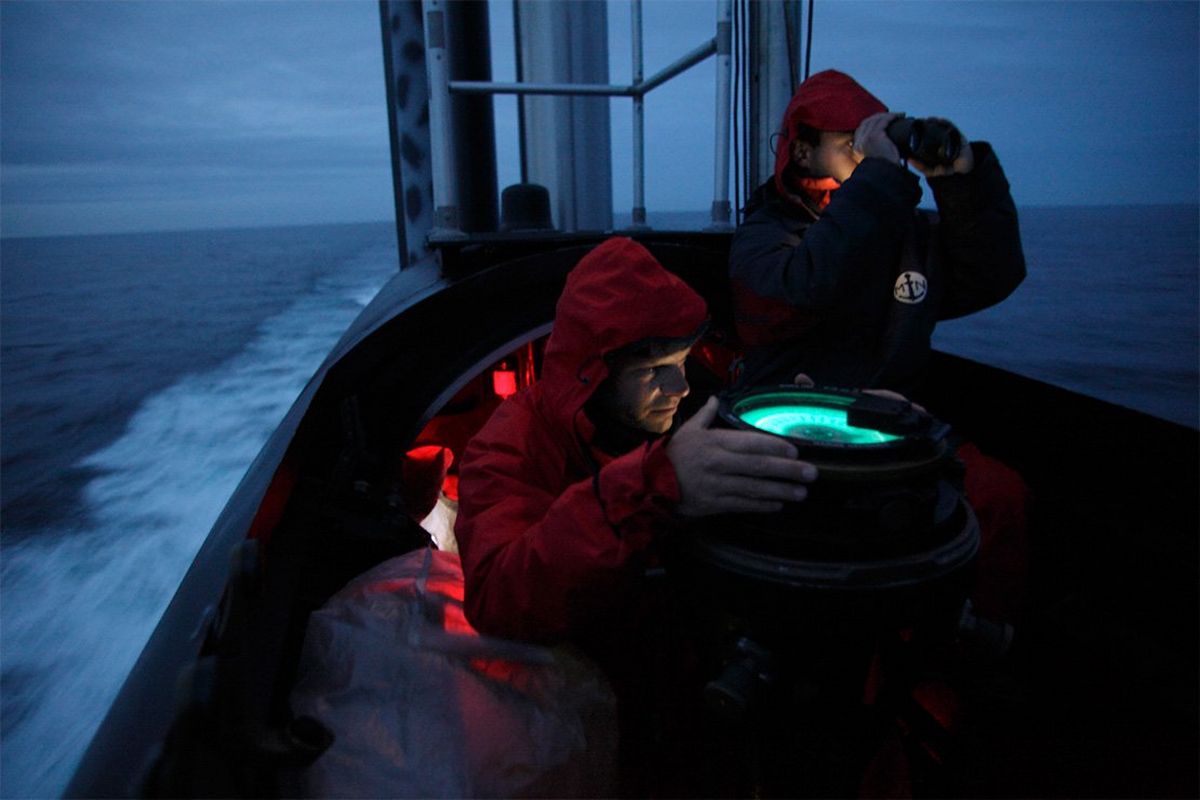 Two crew members on the bridge of a submarine at dusk.