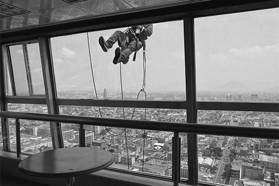A window cleaner outside the 40th floor of the Torre Latinoamericana in Mexico City, with the sprawling city below. Photograph by Jér?me Sessini.