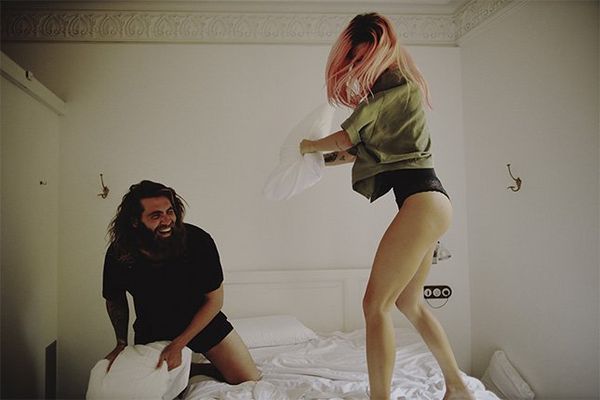 The couple have a pillow fight on a bed wearing pyjamas. 