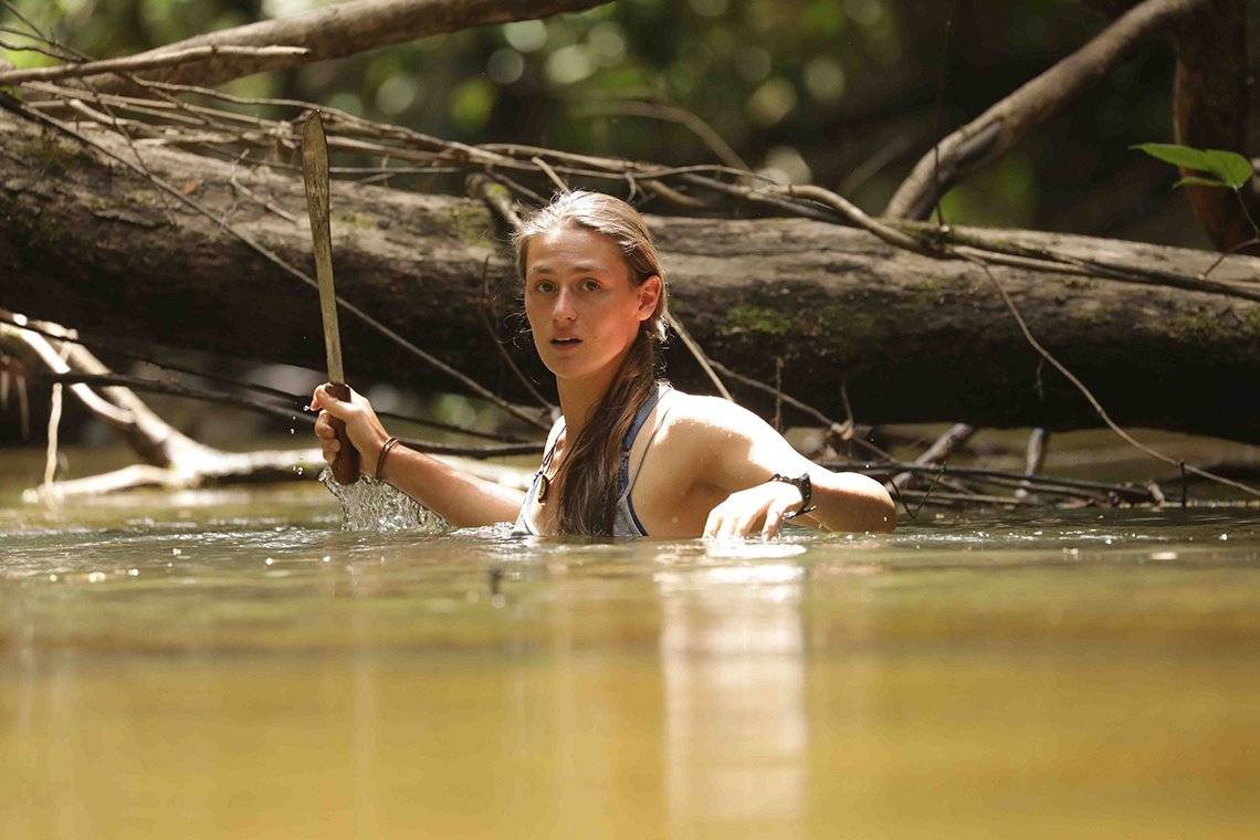 Laura Bingham stands chest-deep in a river, wielding a machete.