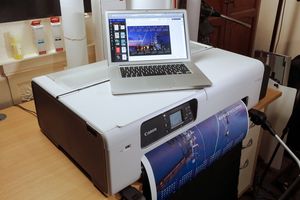 A laptop showing a 2024 calendar created on Canon PosterArtist sits atop a Canon large format printer. A print of the design is emerging from the printer. 