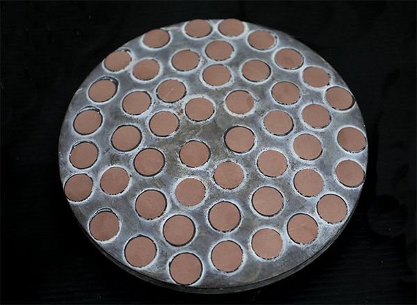 A large, round, indented metal plate is filled with smaller terracotta-coloured discs.